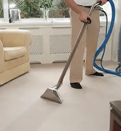 Professional carpet cleaner using a hot-water extraction wand and hose machine in a living room in New Orleans, LA.