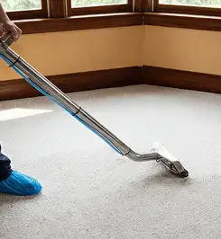 Steam carpet cleaning technician using a hot-water extraction wand on a residential carpet, wearing blue protective shoe covers New Orleans, LA.